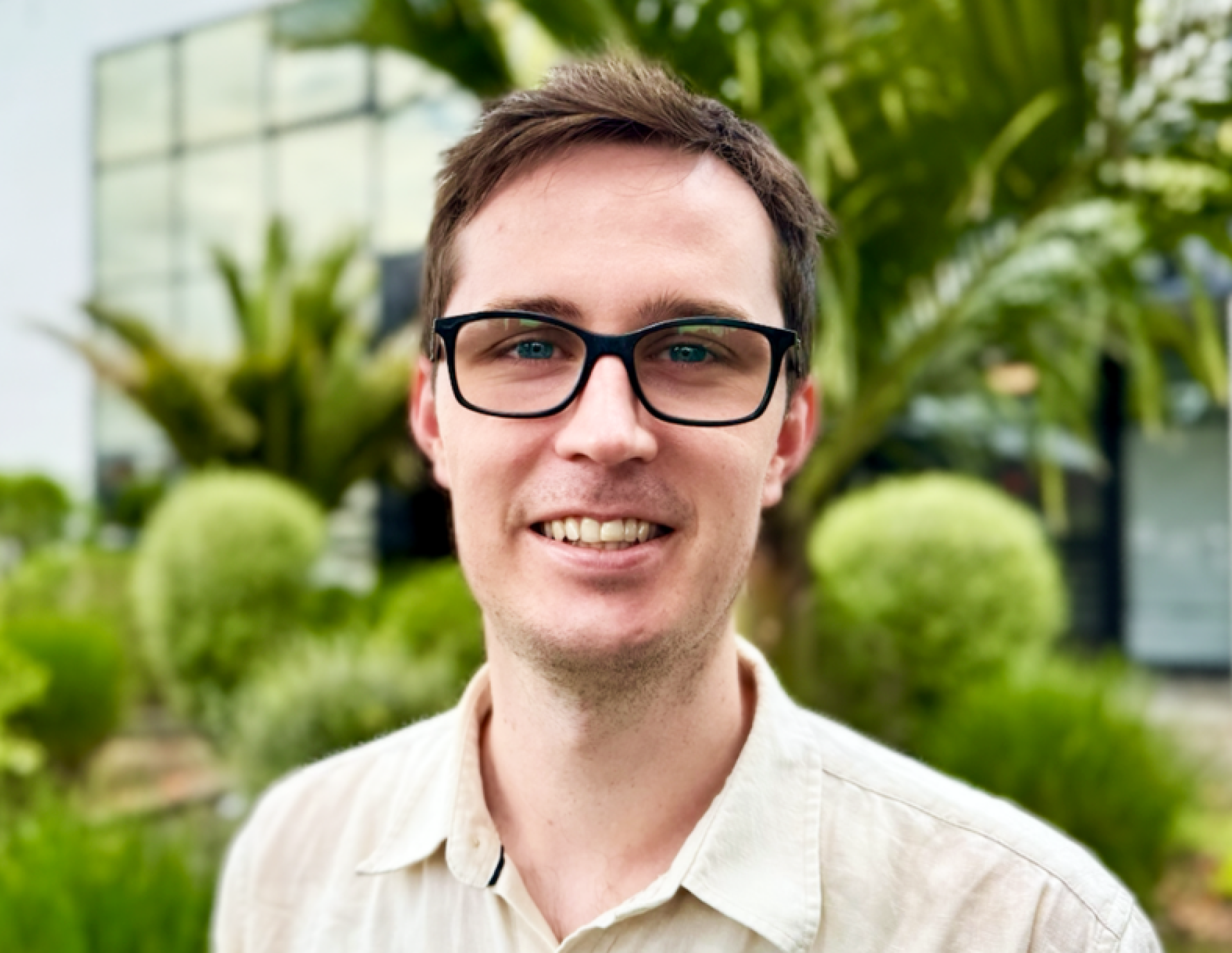 Photo of a person wearing glasses with a backdrop of trees and an office building.